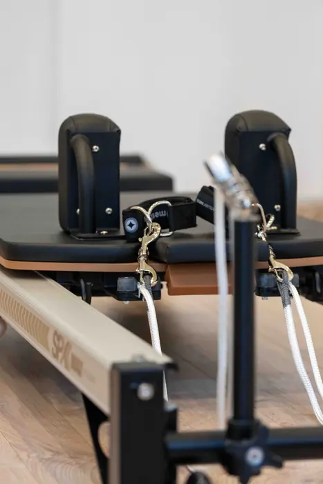 Közeli részlet egy Pilates reformer gépről: vállütközők, hevederek és futószán.